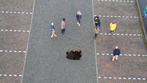 sinkhole in car park with people standing around it