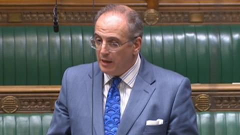 Sir Michael Ellis in light blue suit and blue tie standing up and speaking in the House of Commons