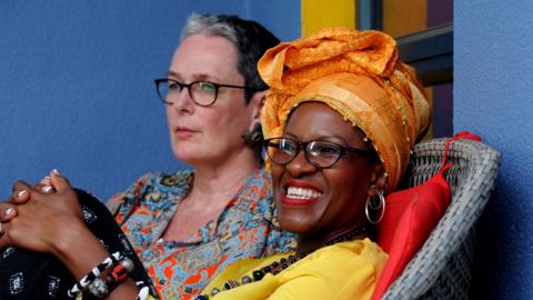 Mpho Tutu van Furth laughs as she sits back on a chair with her wife Marceline in the background.