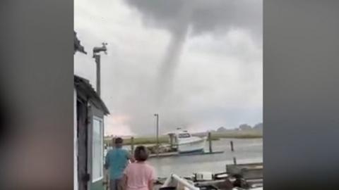 People stand on a dock, looking at the waterspout