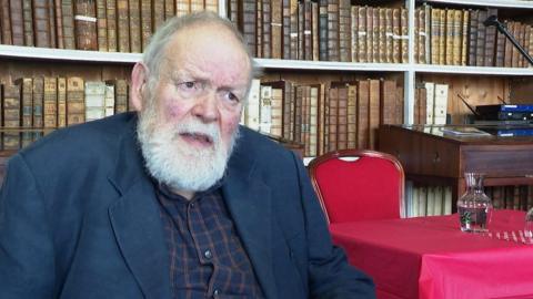 Michael Longley sat in front of books at Armagh library