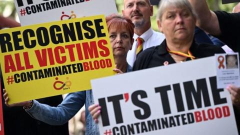 Protestors hold placards with message related to the NHS infected blood scandal as Prime Minister Rishi Sunak gives evidence to the Infected Blood Inquiry in London, on 26 July, 2023