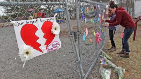A woman and her daughter place a heart on a fence at a growing memorial in front of the Debert School April 20, 2020 in Debert, Nova Scotia, Canada