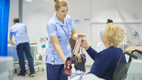 A patient is handed her bag by a nurse