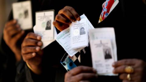 Voters show their voter's identity card as they wait in a queue to cast their vote for the Karnataka state election outside a polling booth in Bangalore on 10 May 2008.