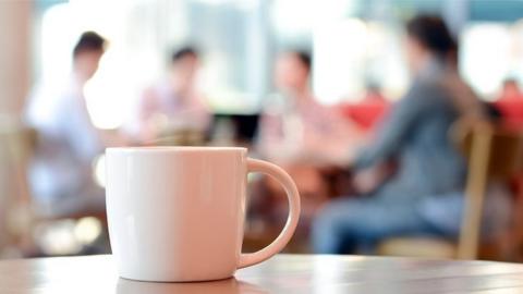 Coffee cup and people meeting in the background