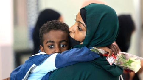 A woman carries a child after fleeing the conflict in Sudan