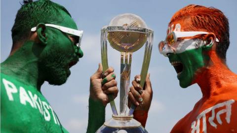 ricket fans, Arun Haryani (Right) and Anil Advani (Left) pose for a photograph with a replica trophy after painting their bodies in the Indian and Pakistani national flag colours, ahead of the match between India and Pakistan in the ICC World Cup, in Ahmedabad, India, October 11,