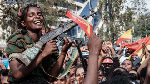 Female soldiers of Tigray Defence Force (TDF) celebrate while they sit on men's shoulders as people celebrate their return on a street in Mekelle