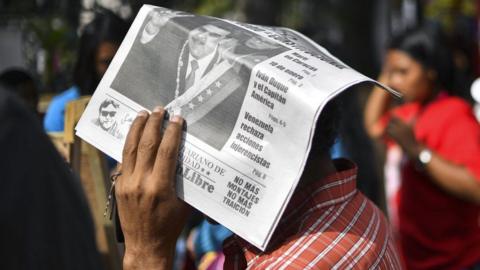 A man protects himself from the sun with a newspaper featuring Venezuelan President Nicolas Maduro, February 2019
