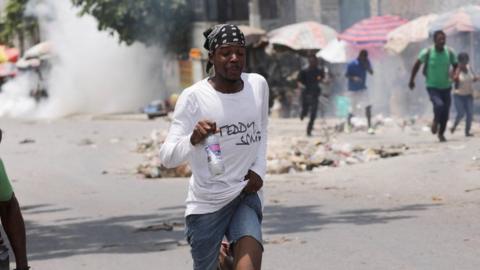 A man runs as police use tear gas near a market in Port-au-Prince, Haiti 24 April