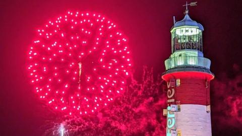 Red Fireworks pictured next to Smeaton's Tower in Plymouth. The tower is a red and white striped lighthouse.