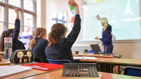 Pupils raise their hands in a classroom