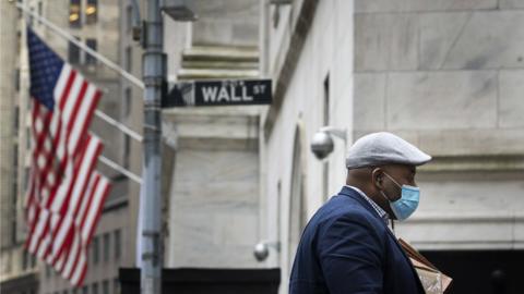 man with mask walks past Wall Street sign