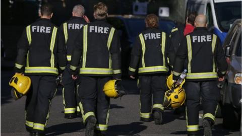 File image of a row of firefighters in uniform walking away from the camera holding their helmets