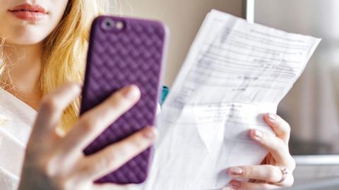 Stock image of a woman using her phone whilst holding a bill