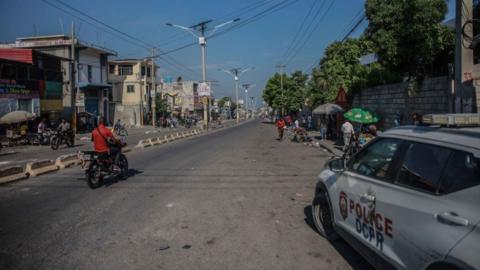 People ride a motorcycle past a police car following a call for a general strike launched by several professional associations and companies to denounce insecurity in Port-au-Prince on October 18, 2021.