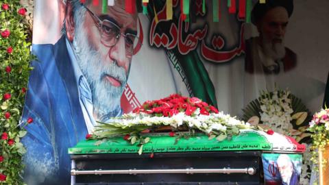 The coffin of Mohsen Fakhrizadeh is displayed in front of a painting of the assassinated nuclear scientist in Tehran, Iran (30 November 2020)