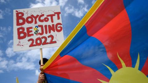 A Tibetan activist holds a placard and a Tibetan flag during a protest against Beijing 2022 Winter Olympics