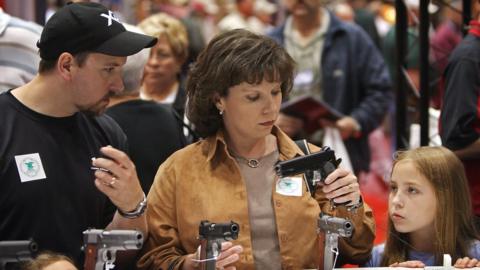 Woman holds gun next to her husband and daughters at the National Rifle Association's May 2008 meeting