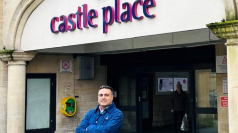 Tahir Ali smiling with arms folded across his chest, while standing outside Castle Place Shopping Centre