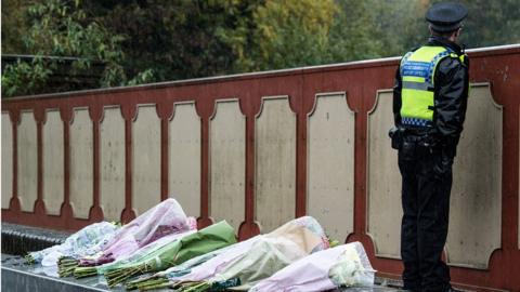 A police officer stands next to flowers on a bridge that overlooks Croydon tram crash site