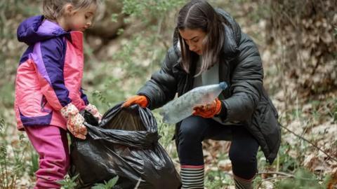 Woman and young girl picking up litter, both holding a black bin bag while outside