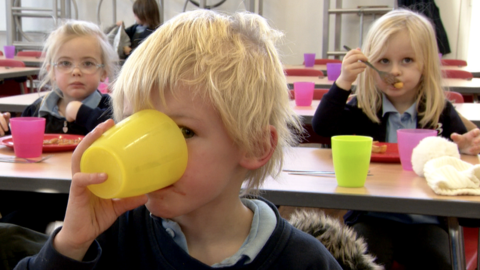 Child drinking water from a yellow plastic glass