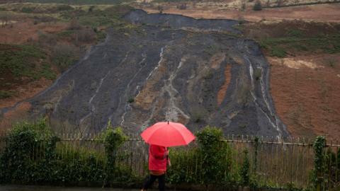 Landslip on coal tip at Tylorstown, woman with umbrella in front