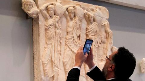 A visitor takes a photo of one of three Parthenon fragments, returned from the Vatican