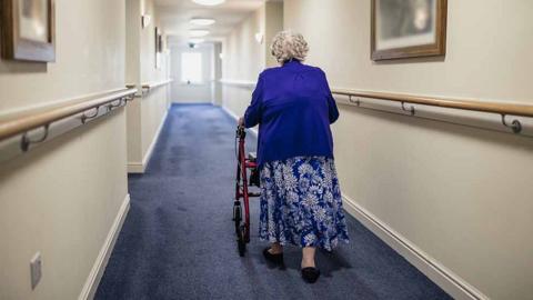 old lady walks down corridor in care home