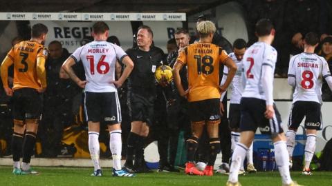 Players from both teams are taken off the pitch by the referee