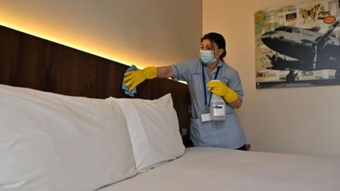 A member of the cleaning staff cleans surfaces as she prepares a room for a guest at the St Giles Hotel, near Heathrow Airport