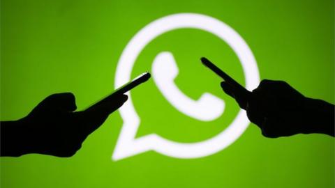 Two people use their smartphones in front of a large WhatsApp logo