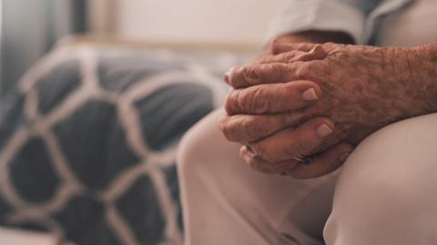 Elderly woman sitting with her hands clasped in a retirement home