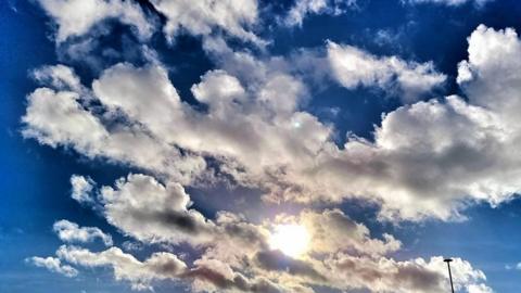 The sun shining through fluffy white clouds in a very blue sky