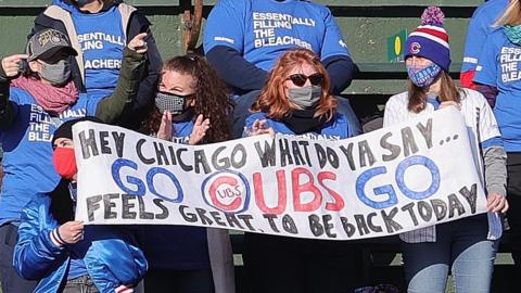 Socially-distanced fans wearing masks hold up a banner in support of the Chicago Cubs at their 2021 season opener against the Pittsburgh Pirates at Wrigley Field