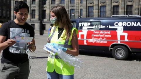 A woman hands out masks and information brochures in Amsterdam, Netherlands August 5, 2020