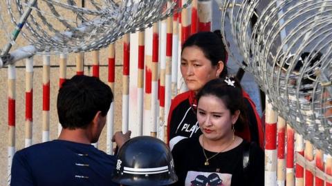 A file photo from 2019 showing Uygher women going through the entrance to a bazaar in Hotan, Xinjiang, past police officers and a gateway covered in razor wire