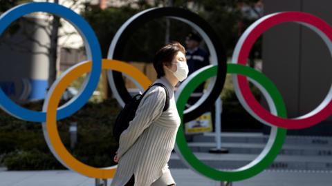 A woman wearing a protective mask walking in front of Olympic rings at the Olympics Museum in Tokyo