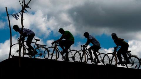 Spectators ride stationary bicycles atop a recreational vehicle along the route of the fifth stage of the 105th edition of the Tour de France