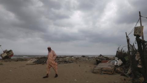 A boat maker walks with the rain clouds in the background, before the arrival of cyclonic storm.