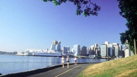 Wide shot of Stanley Park, with sea and Vancouver skyline in the background