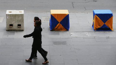 Women walk past decorated concrete bollards in Melbourne