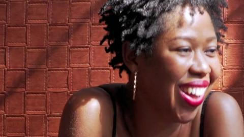 A woman smiles in front of a brick wall