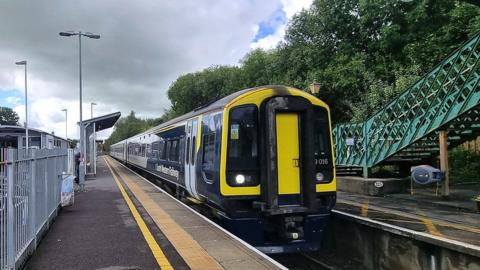 a black, navy and yellow South Western Railway train at the platform at Templecombe Station
