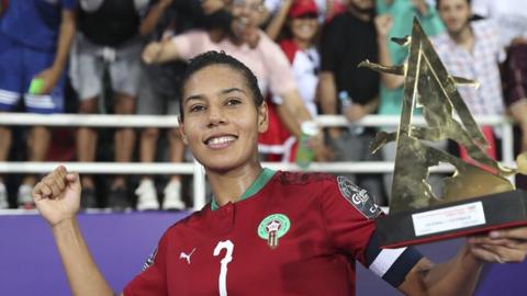 Ghizlane Chebbak in Morocco kit holds up a trophy and poses in front of fans