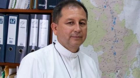 Bishop Barreto poses next to a map