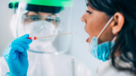 woman in mask being swabbed by person in visor