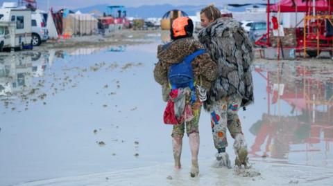 Dub Kitty and Ben Joos, of Idaho and Nevada, walk through the mud at Burning Man after a night of dancing with friends in Black Rock City, in the Nevada desert